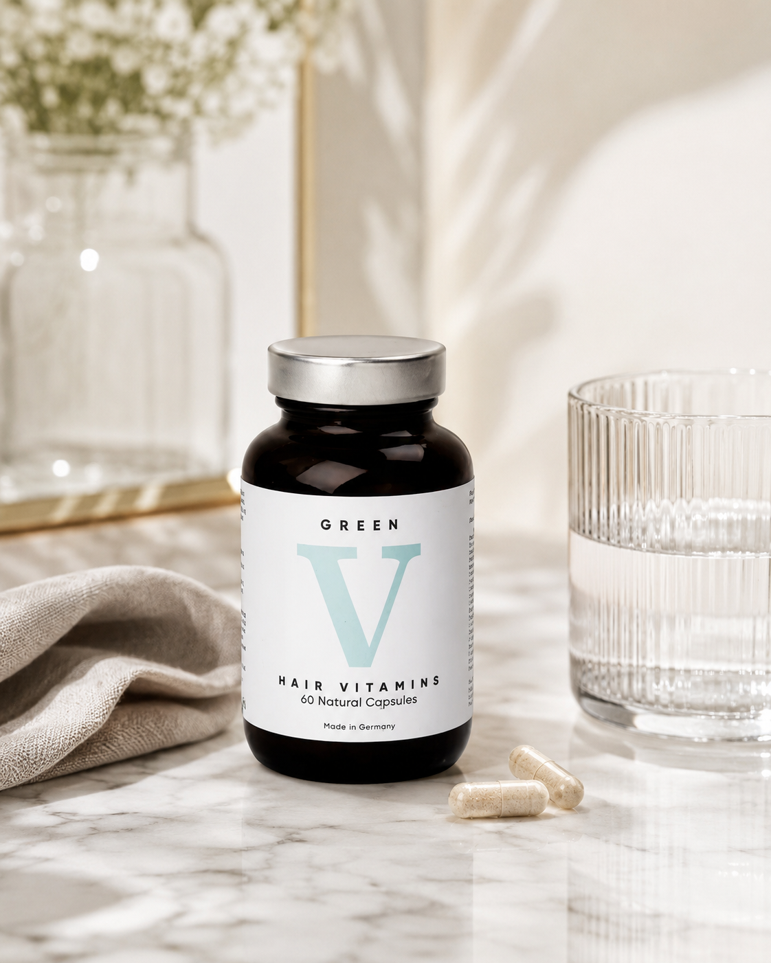 Green V Hair Vitamins bottle on a marble surface with capsules